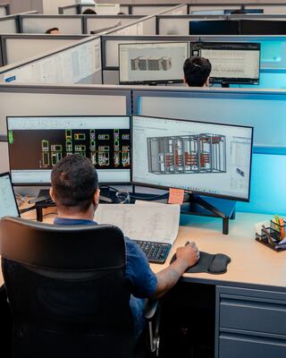 Two IEM employees sitting at desks, working on engineering files at their computers.