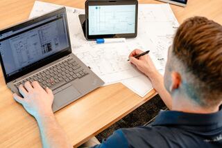 An IEM employee working on engineering drafts at a desk